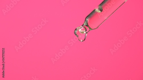 Oil or liquid dropper or pipette in extreme macro close up. Drop of yellow cosmetic lavender oil falling on pink background. Eyedropper squeezing out meds droplets.