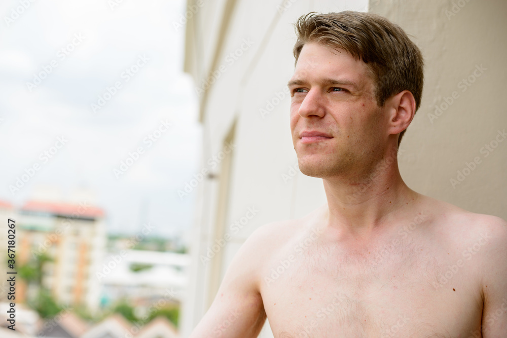 Young handsome shirtless man against view of the city with nature