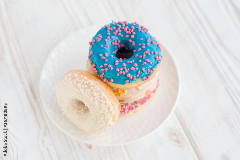Close-up view of stack of four colored donuts on a small white plate with white background. Fresh sweet homemade vanilla donuts on wooden background for birthday or party, with free space for text Close-up view of stack of four colored donuts on a small white plate with white background. Fresh sweet homemade vanilla donuts on wooden background for birthday or party, with free space for text
