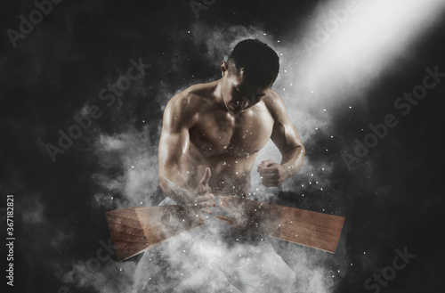Karate man breaking with hand wooden board on smoke background. Sports banner