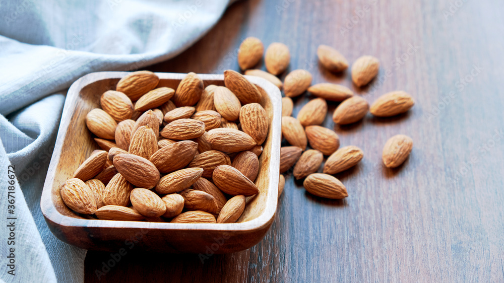 Almonds in small wooden bowl. Almonds laid freely on dark table. Row of bowls with almond nuts, top view. Peeled almond pattern Almonds in small wooden bowl. Almonds laid freely on dark table. Row of bowls with almond nuts, top view. Peeled almond pattern