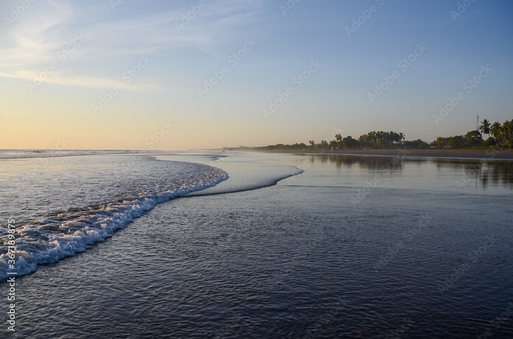 Fototapeta premium Tranquil beach in Nicaragua without people during sunset. Sea landscape with blue and orange sky. Shore view of the sea water with small waves