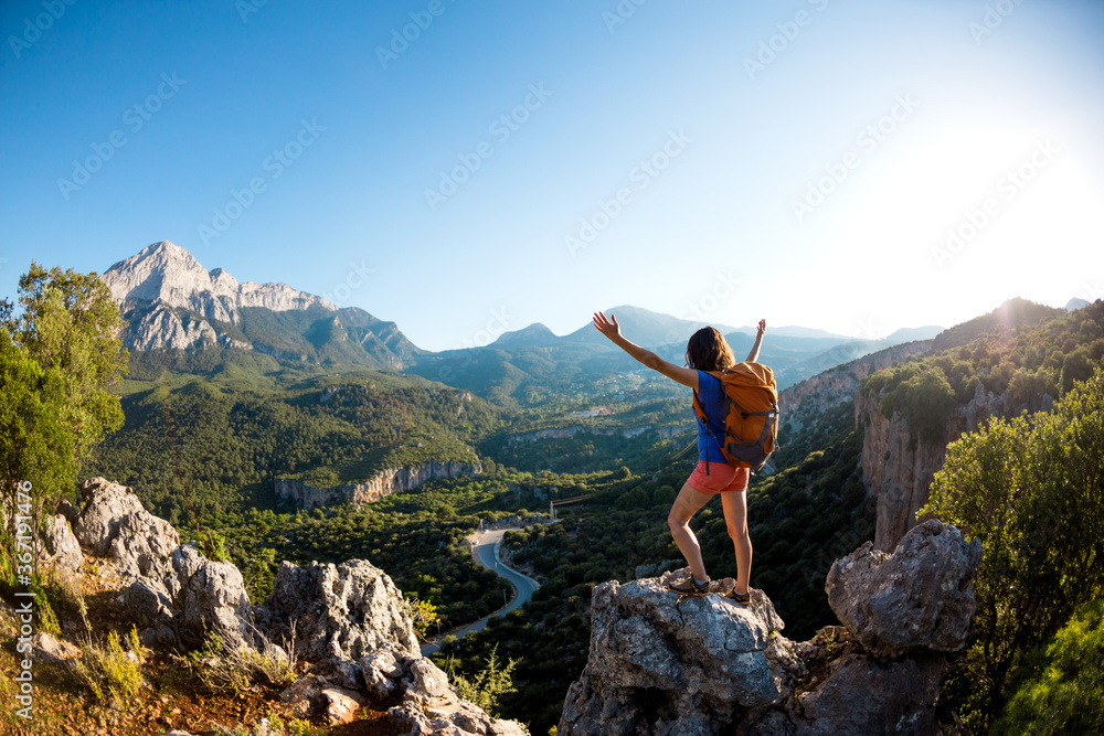 A woman with a backpack stands on top of a mountain and admires the beauty of a mountain valley. A woman with a backpack stands on top of a mountain and admires the beauty of a mountain valley.