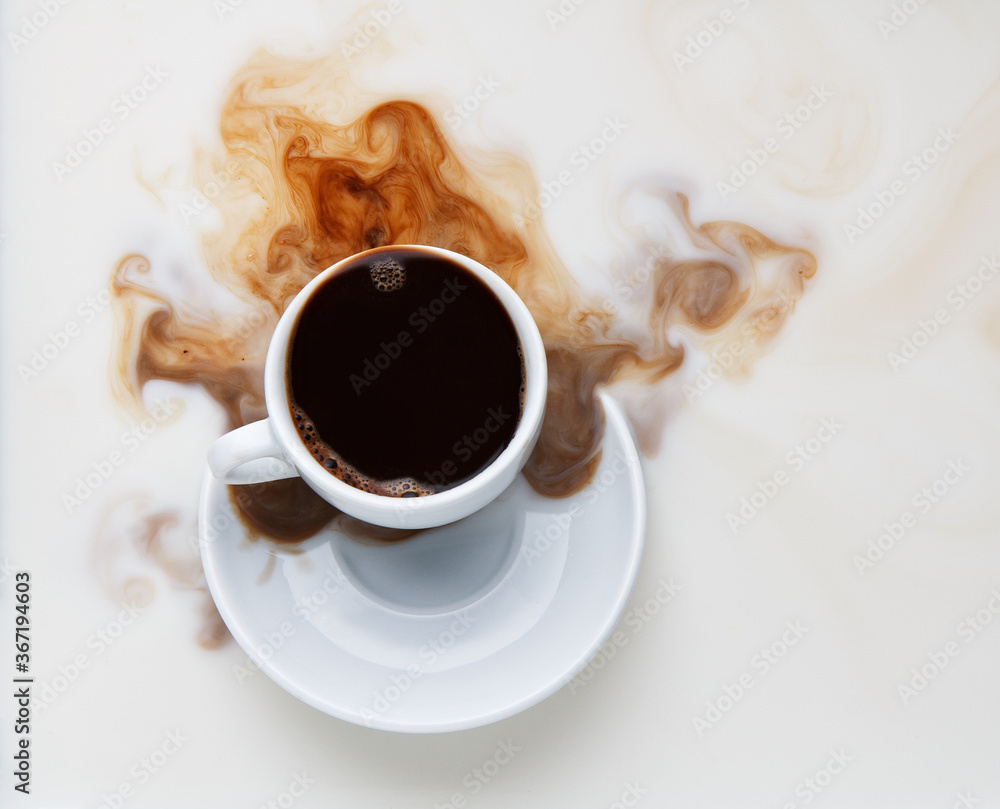 black coffee pouring from a white cup into milk - obrazy, fototapety, plakaty 