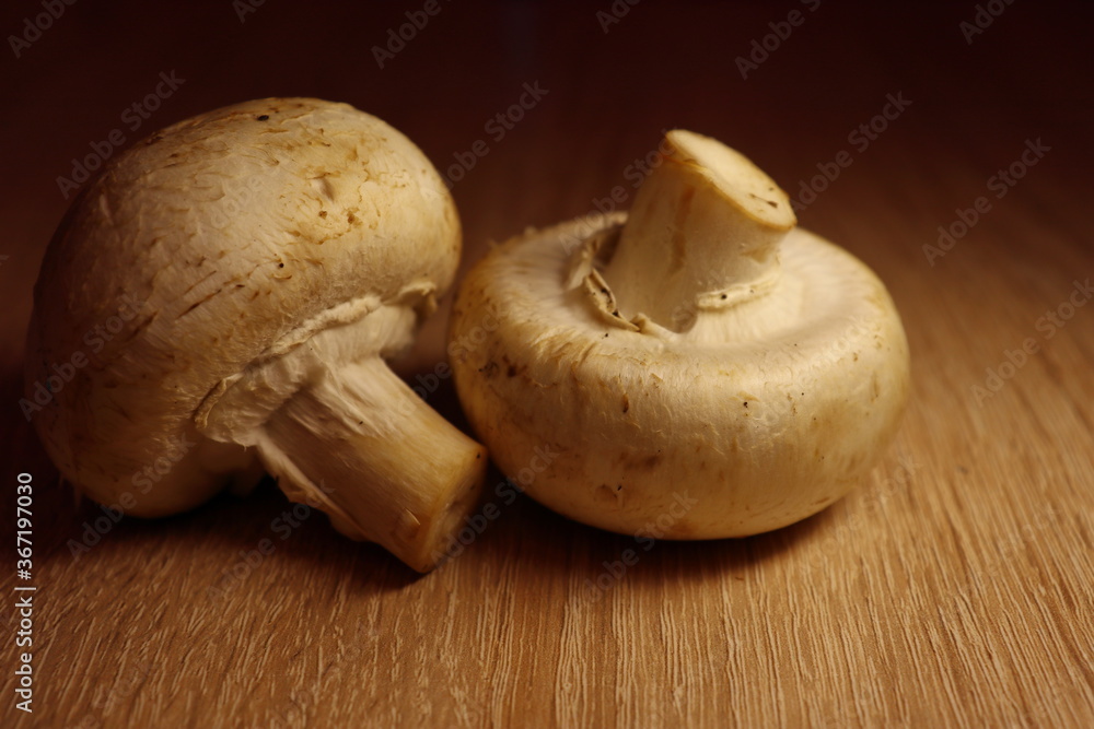 Two mushrooms on the wooden table. Close up view. Dark background. Two mushrooms on the wooden table. Close up view. Dark background.