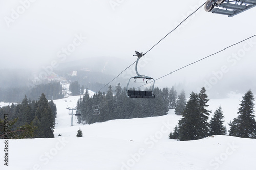 Chair lift in the snowy mountain summit, pine trees and fog. Winter tourism concept. Trip in winter season.