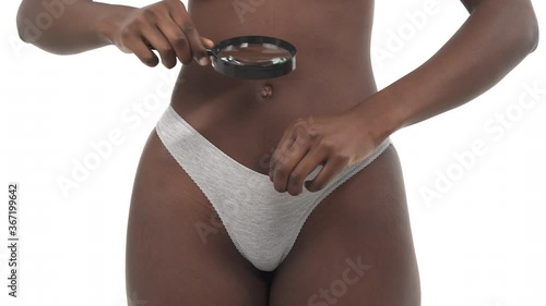 Lower body of black woman looking into her panties through magnifying glass. Isolated on white background