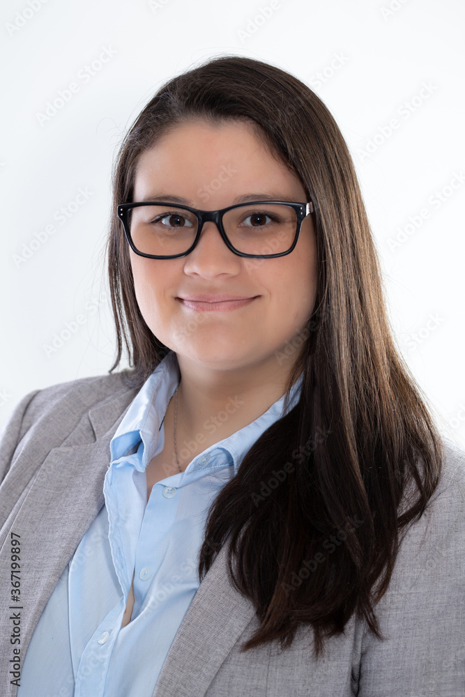 Young businesswoman poses for a studio portrait. She is in her early thirties, She is wearing a gray suit, blue shirt and prescription glasses. She is smiling.
