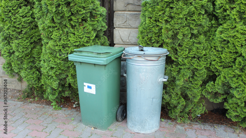 Two waste plastic containers with waste near the fence in the yard of a private house. Separate waste sorting. Responsible attitude to the environment.