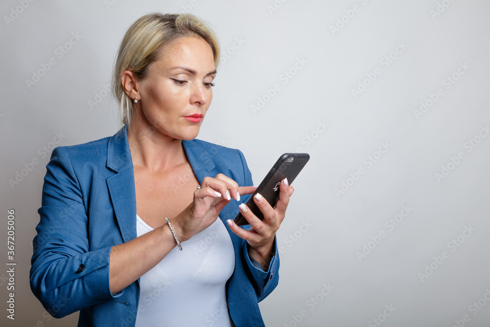 Naklejka premium Young woman, blonde hair, writes in a smartphone sms, studio, white background