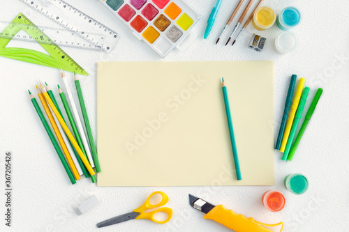 Blank yellow sheet of paper with colored school supplies