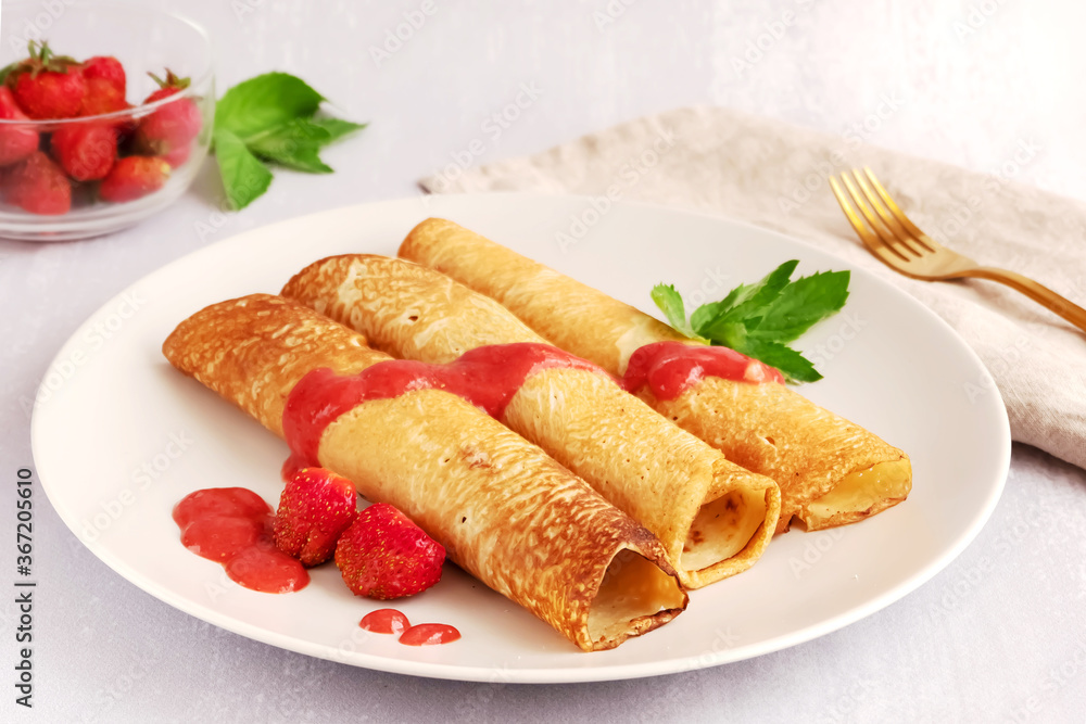 Three delicious crepes covered with strawberry sauce and strawberries on a plate, light grey background Three delicious crepes covered with strawberry sauce and strawberries on a plate, light grey background