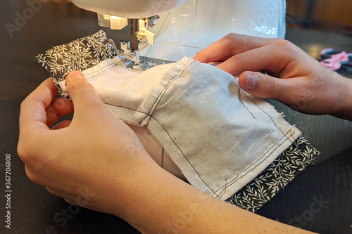 Closeup of hands stitching seam in homemade mask using sewing machine