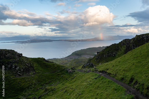A rainbow arches over the mountains in the distance. Hiking trail to the majestic rock pinnacle of the Old Man of Storr.