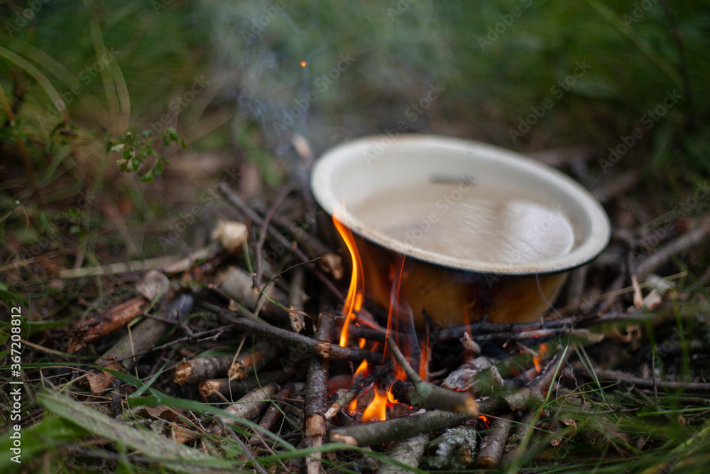 A metal bowl of water is heated over a fire. A metal bowl of water is heated over a fire.