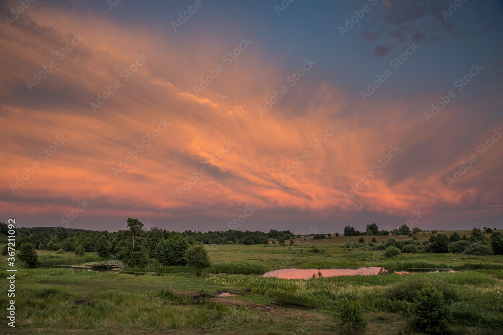 Dramatic red evening clouds over the meadow and the river.