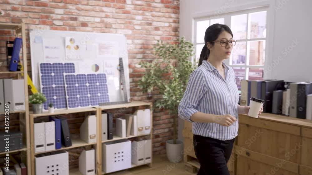 asian japanese lady worker working on construction plan in office. woman architect stand in back by whiteboard with green energy building document on it. designer walking to seat with cup of coffee asian japanese lady worker working on construction plan in office. woman architect stand in back by whiteboard with green energy building document on it. designer walking to seat with cup of coffee