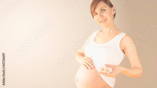 Pregnant young woman with pregnancy week number next to her belly. Photos of belly growth at 32 weeks pregnancy. Healthy pregnancy diet and fetal development. photo