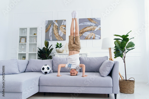Obraz na plátně Sporty acrobat boy standing on his head on sofa at home.