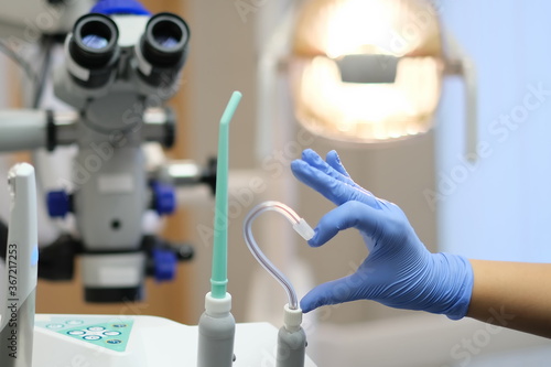 Fototapeta Naklejka Na Ścianę i Meble -  Hand in Blue latex glove and saliva ejector in shape of heart and dental microscope on beckground