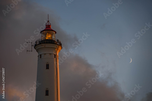 Lighthouse in the evening with clouds. The beacon of of  Lyngvig lighthouse of Holmsland Klit on the west coast of Jutland, by Hvide Sande, Denmark  with blue cloudy sunset sky and moon
 photo