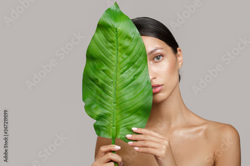 Portrait of a woman and green leaves. Organic beauty. Gray Background Copycpase