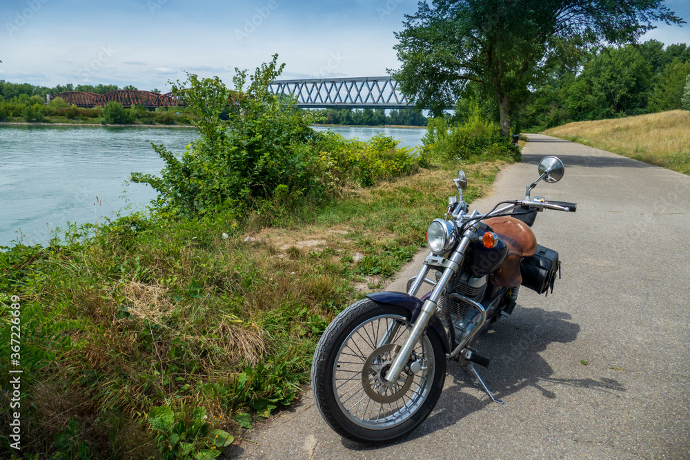 Motorrad steht einsam am Rhein, Im Hintergrund die alte Brücke Wintersdorf Motorrad steht einsam am Rhein, Im Hintergrund die alte Brücke Wintersdorf