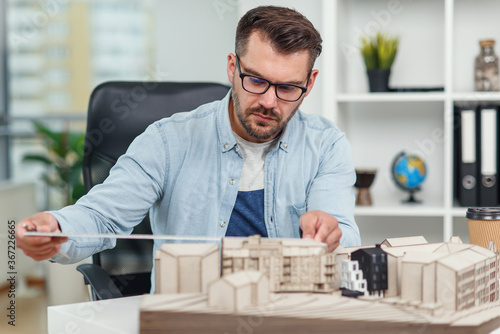 Handsome caucasian senior architect at glasses working on a construction project and examines the model on which he works.