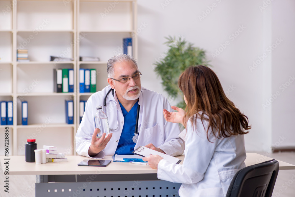 Old male doctor and his young female assistant in the clinic Old male doctor and his young female assistant in the clinic
