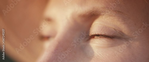 Close up portrait of a young gardener or farmer woman eyes looking up at beautiful evening sunset sunlight golden light wear a hat macro slow motion photo
