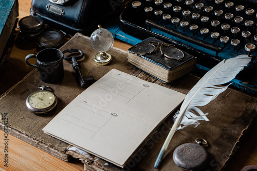  old mood board wooden table with accessories: a manual typewriter, an ink pen, an old pocket watch, vintage glasses and an old textured blank business card, flat lay