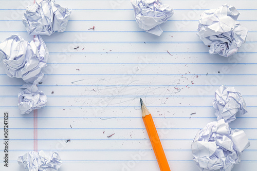 School supplies of blank lined notebook paper with eraser marks and erased pencil writing, surrounded by balled up paper and a sharp pencil. Studying or writing mistakes concept. photo