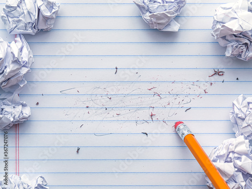 School supplies of blank lined notebook paper with eraser marks and erased pencil writing, surrounded by balled up paper and a pencil eraser. Studying or writing mistakes concept. photo