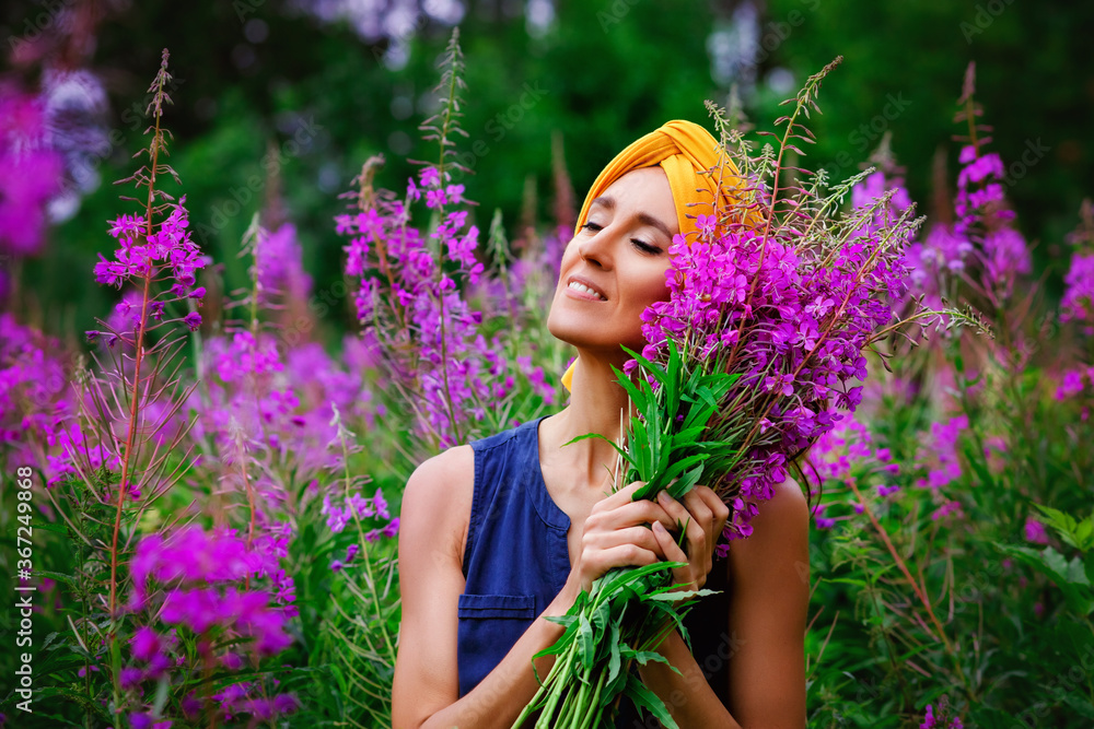 A young beautiful girl collects flowers in a field. A woman walks and enjoys a field of flowers with her eyes closed. A bouquet of pink flowers of narrow-leaved cypress Ivan-tea. A young beautiful girl collects flowers in a field. A woman walks and enjoys a field of flowers with her eyes closed. A bouquet of pink flowers of narrow-leaved cypress Ivan-tea.