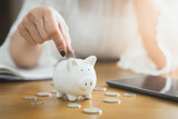 Woman inserts a coin into a piggy bank, financial concept