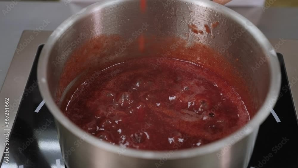 Close-up of a professional chef preparing strawberry jelly or marmalade for a cake. Strawberry jelly boils in a saucepan, the cook stirs the berry jelly with a silicone spatula. Close-up of a professional chef preparing strawberry jelly or marmalade for a cake. Strawberry jelly boils in a saucepan, the cook stirs the berry jelly with a silicone spatula.