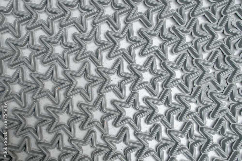 A fragment of a doormat consisting of raised contours of rubber black stars fused into a single structured pattern, lying on a gray concrete floor. Modern geometric synthetic abstract background. A fragment of a doormat consisting of raised contours of rubber black stars fused into a single structured pattern, lying on a gray concrete floor. Modern geometric synthetic abstract background.