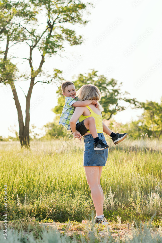 Young cheerful family in the meadow. Mom and son schoolboy spend time together and have fun in nature. Leisure. Summer holidays. Summertime. Happy childhood and motherhood