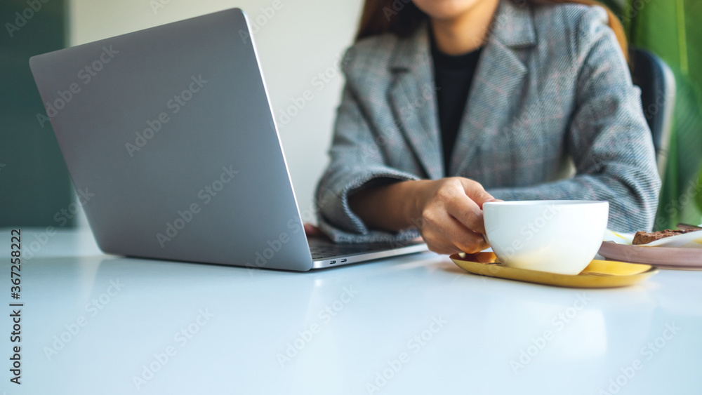 Closeup image of a business woman using and working on laptop computer while drinking coffee in office Closeup image of a business woman using and working on laptop computer while drinking coffee in office