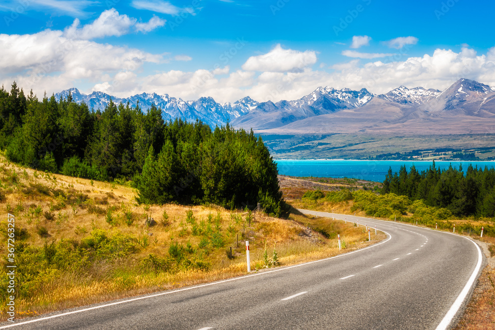 Fototapeta premium Mount Cook State Highway in New Zealand's South Island is one of the most picturesque alpine roads in the world. Winding road perspective with lake Pukaki and snow-capped mountains in the background.