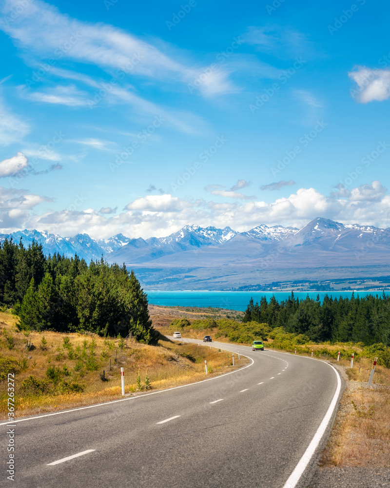 Mount Cook State Highway in New Zealand's South Island is one of the most picturesque alpine roads in the world. Winding road perspective with Lake Pukaki and snow-capped mountains in the background.
