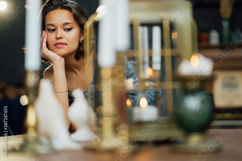 portrait of beautiful young brunette through candles on wooden table. 