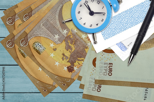 50 euro bills and alarm clock with pen and envelopes. Tax season concept, payment deadline for credit or loan. Financial operations using postal service photo