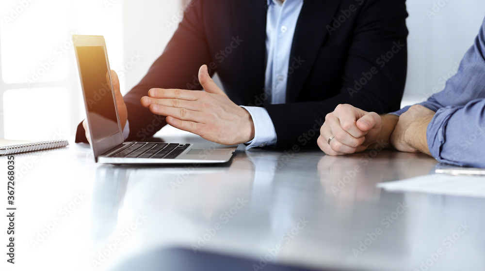 Business people using laptop computer while working together in sunny modern office. Unknown businessman with colleague at workplace. Teamwork and partnership concept Business people using laptop computer while working together in sunny modern office. Unknown businessman with colleague at workplace. Teamwork and partnership concept