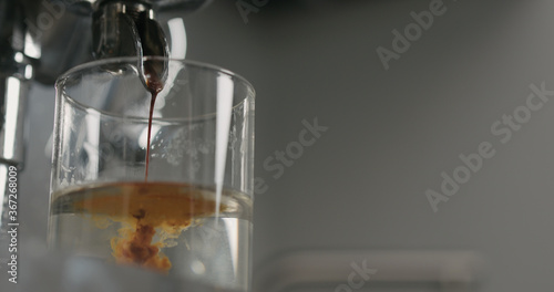 low angle pour from coffee machine into glass with water