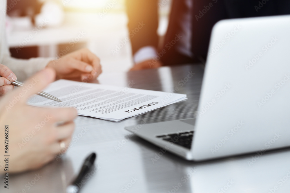Business people discussing contract while working together in sunny modern office. Unknown businessman and woman with colleagues or lawyers at meeting Business people discussing contract while working together in sunny modern office. Unknown businessman and woman with colleagues or lawyers at meeting