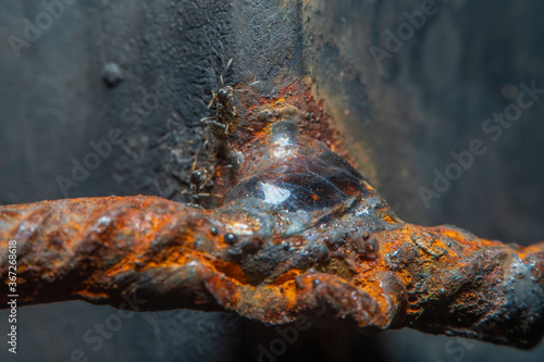 A close-up of the weld of an iron rod to a rusty metal structure. Highly magnified with soft focus weld metal assembly