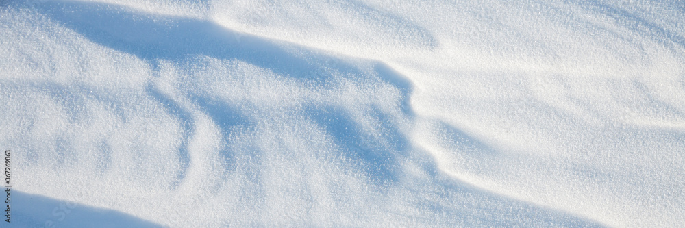 Obraz premium Beautiful winter background with snowy ground. Natural snow texture. Wind sculpted patterns on snow surface. Wide panoramic texture for background and design.
