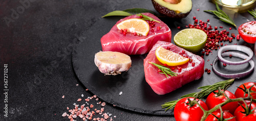 Fresh tuna fillet steaks with spices and herbs on a black background
