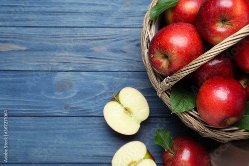 Juicy red apples in wicker basket on blue wooden table, flat lay. Space for text